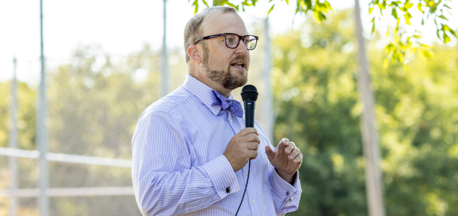 Bearded Man holding microphone while wearing purple